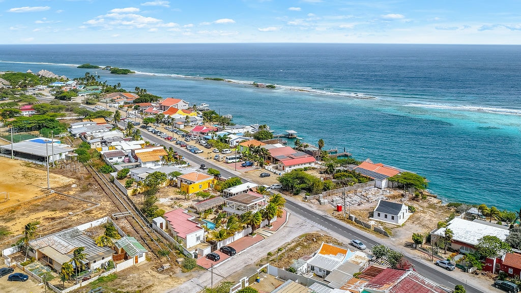 Aerial view of the Savaneta coastline in Aruba, with colourful houses along the road and turquoise water beyond.
